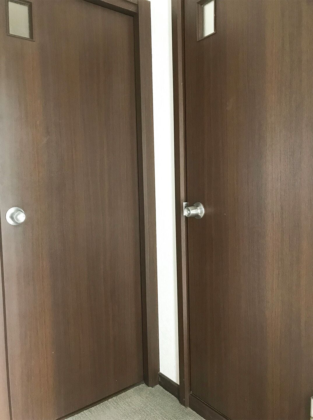 A closed wooden door with a silver handle and a small rectangular window at the top.