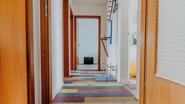Un pasillo con puertas de madera, un suelo colorido y un televisor al fondo.