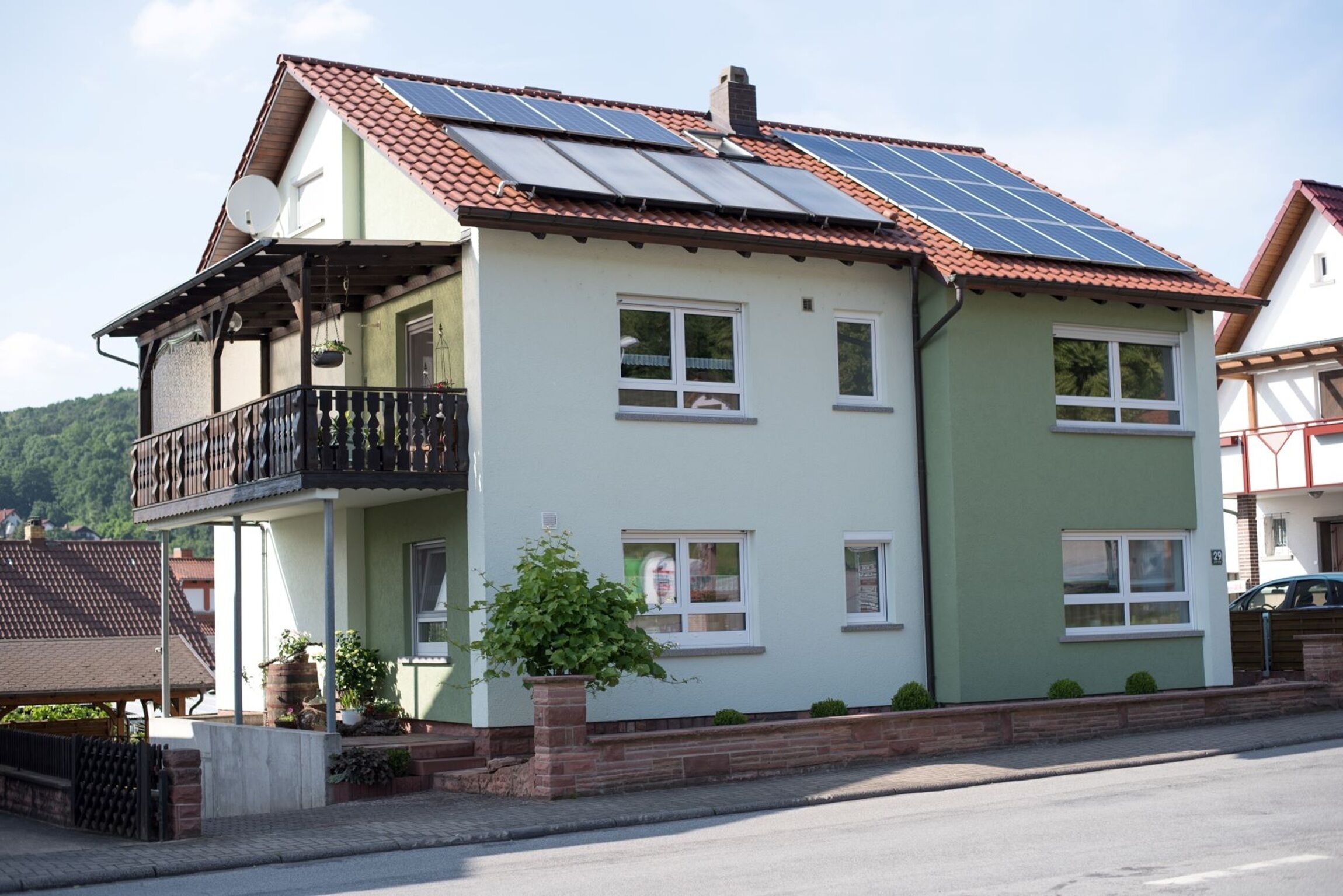 A two-story house with a balcony, solar panels on the roof, and a small garden area.