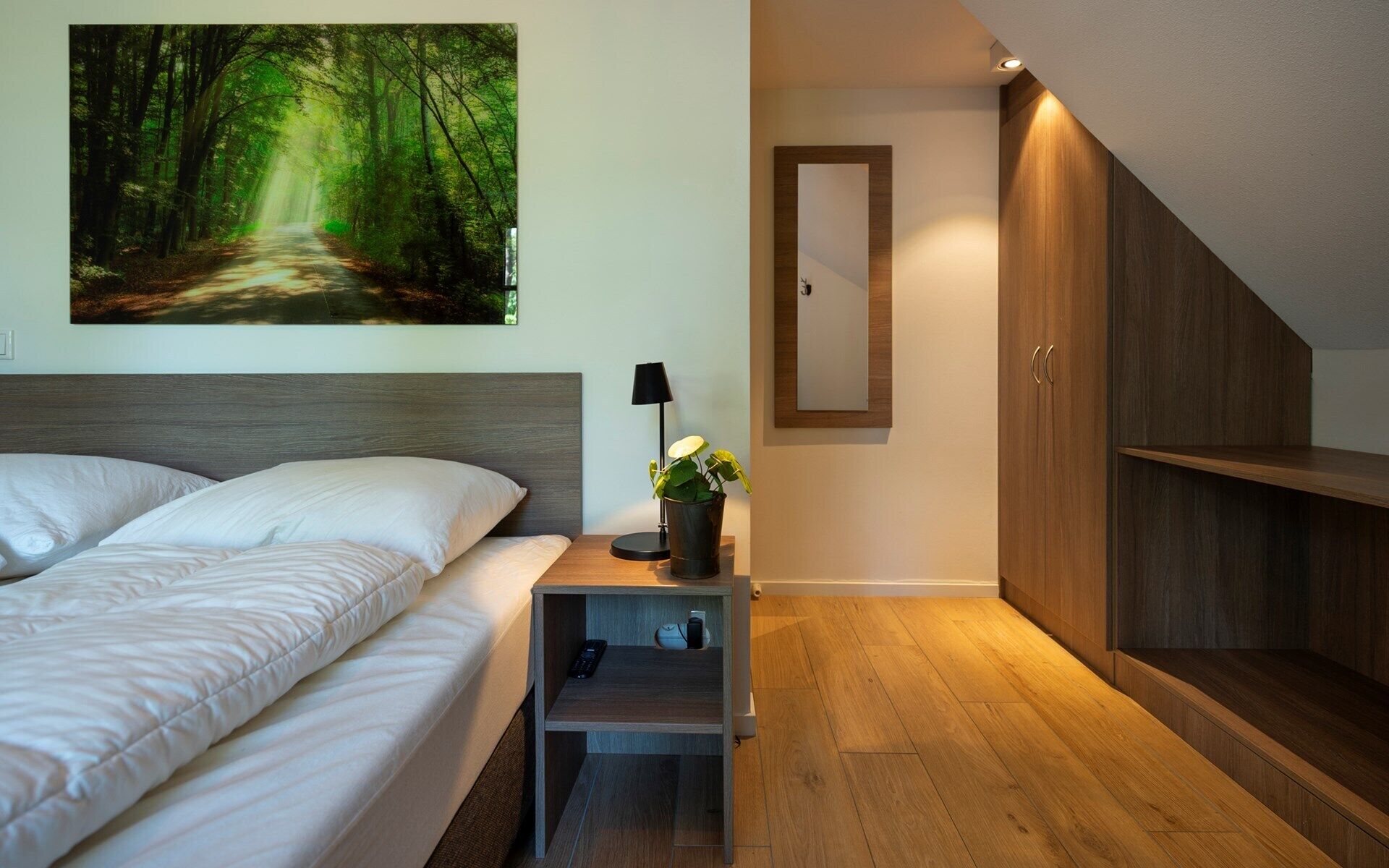 A bedroom with a bed, bedside table, lamp, and a mirror.