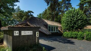 A rustic wooden building with a thatched roof, labeled with the number 14, surrounded by lush greenery.