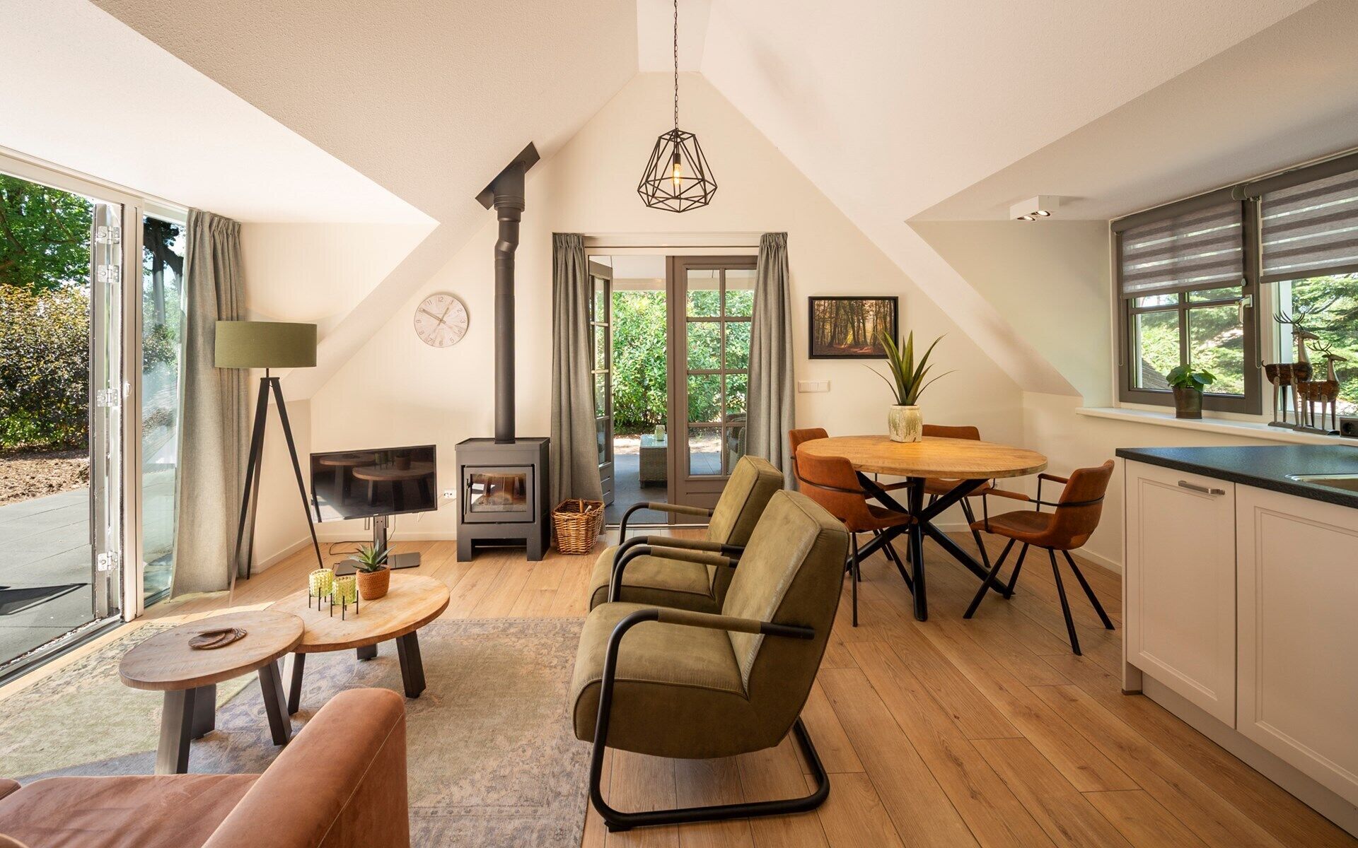 A spacious loft with a high ceiling, a wood-burning stove, a dining area with a round table, and a kitchen with a large window.