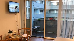 A small, modern room with a bed, a TV, a table with chairs, and a balcony with a table and chairs.