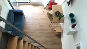 A modern living room with a blue sofa, wooden flooring, a dining area with a table and chairs, and a staircase.
