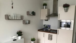 A modern kitchen with white cabinetry, a wooden countertop, a built-in microwave, and potted plants.