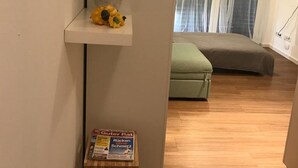 A modern apartment with a wooden floor, a green sofa, a potted plant, and a magazine on a small wooden stool.