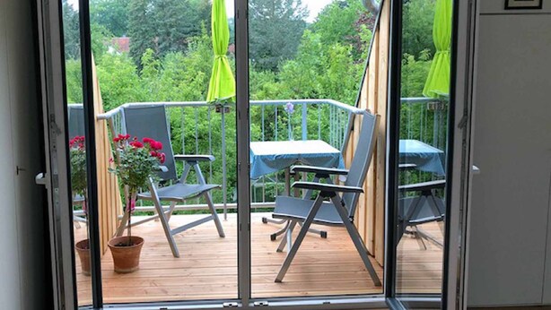 Een kamer met een schuifglazen deur naar een terras buiten, compleet met stoelen en een tafel.