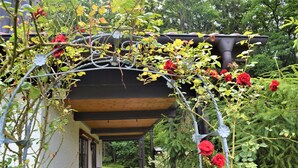 A covered outdoor seating area with chairs and a table, surrounded by lush greenery and red flowers. - Feriendorf Büchelberg (Windorf)