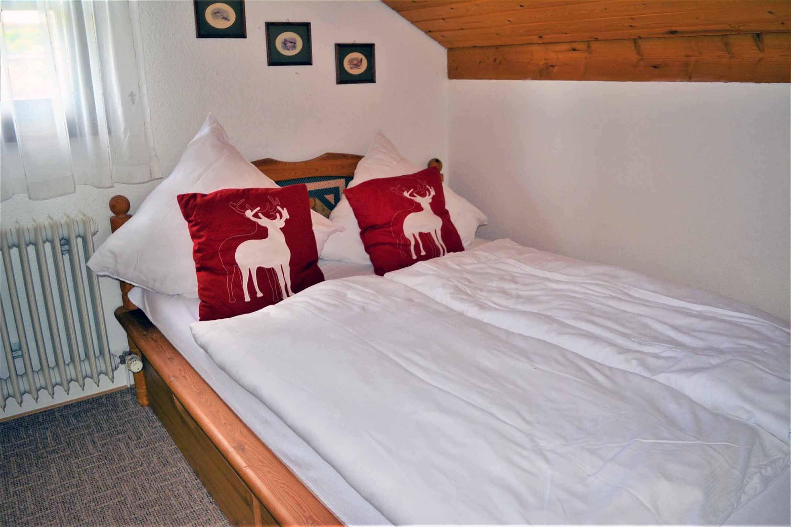 A bed with white bedding and two red pillows with deer designs.