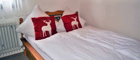 A bed with white bedding and two red pillows with deer designs.