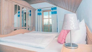 A bedroom with a wooden ceiling, a bed with white bedding, a lamp, and a window with curtains. - Feriendorf Büchelberg (Windorf)