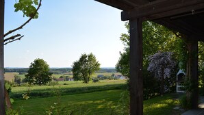 A covered outdoor area with a view of a green field and trees. - Feriendorf Büchelberg (Windorf)