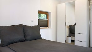 Une chambre à coucher avec un lit, une fenêtre avec des stores, un miroir et une armoire.