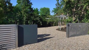 Un chemin de gravier mène à une entrée fermée par un portail, avec une pergola en arrière-plan.