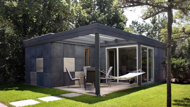 Un espace extérieur moderne et clos, doté d’un patio, de sièges et d’une porte vitrée donnant sur un jardin.