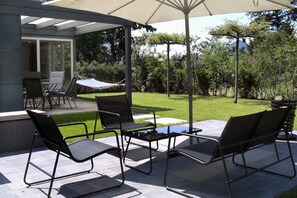 An outdoor patio with a covered seating area, a hammock, and a view of a well-maintained lawn and trees. - Cube-House Ferienhaus in Franken (Volkach)