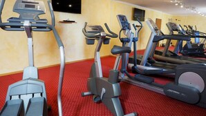 A gym with multiple treadmills and elliptical machines, a red carpet floor, and a television mounted on the wall.