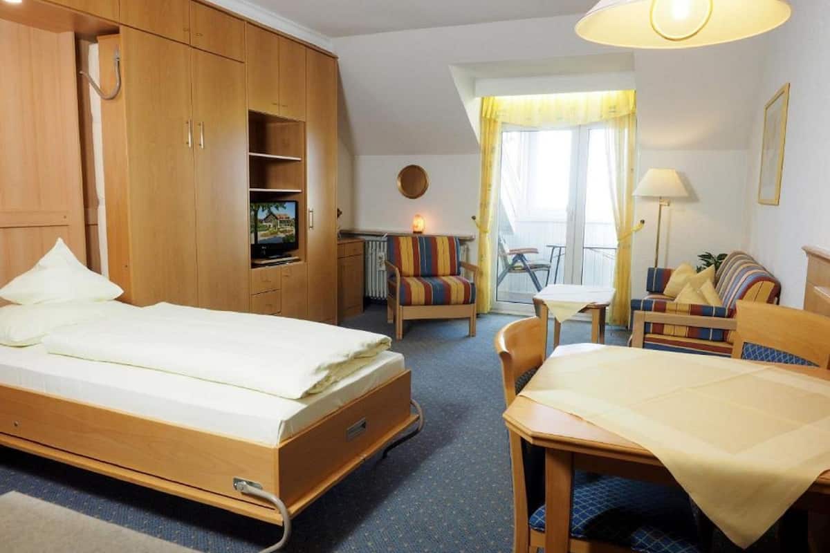A hotel room with a bed, a desk, a chair, a sofa, and a TV.