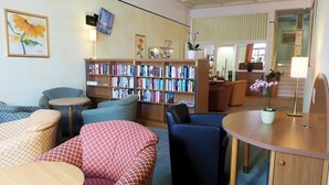 A cozy lounge area with patterned sofas, a wooden coffee table, and a bookshelf filled with books.