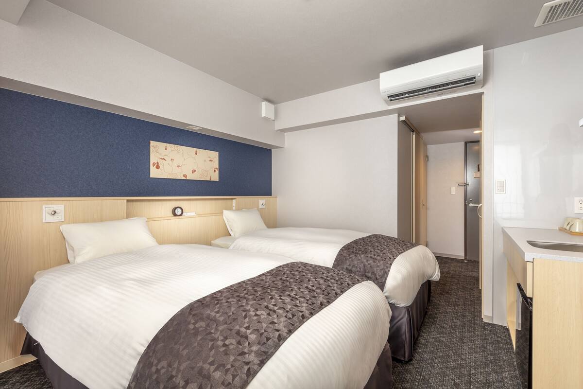 Une chambre d’hôtel avec deux lits, une petite kitchenette et un appareil de climatisation.
