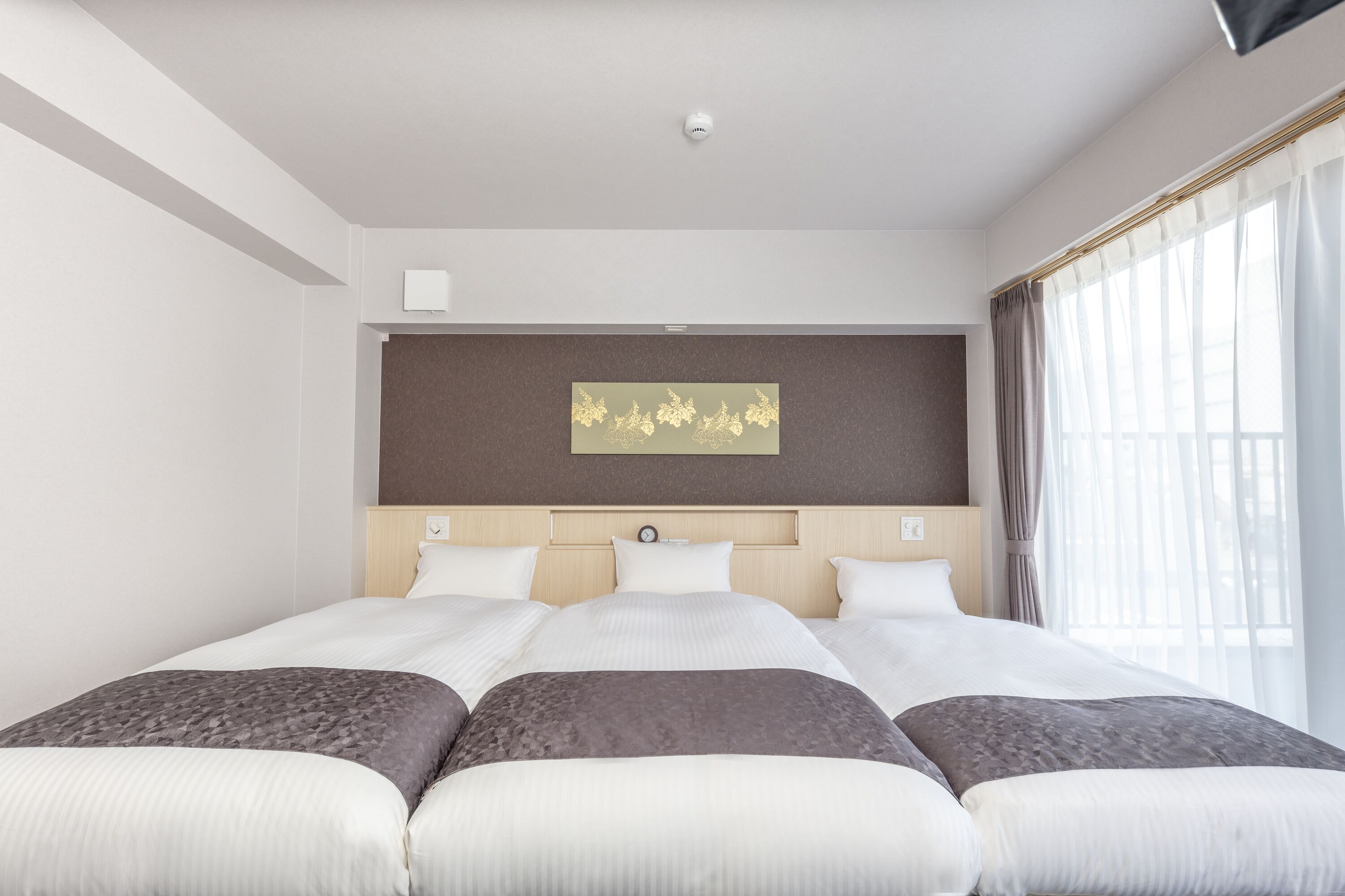 Hotelkamer met een groot bed, een hoofdeinde met een klok, een kunstwerk aan de muur en een raam met gordijnen.