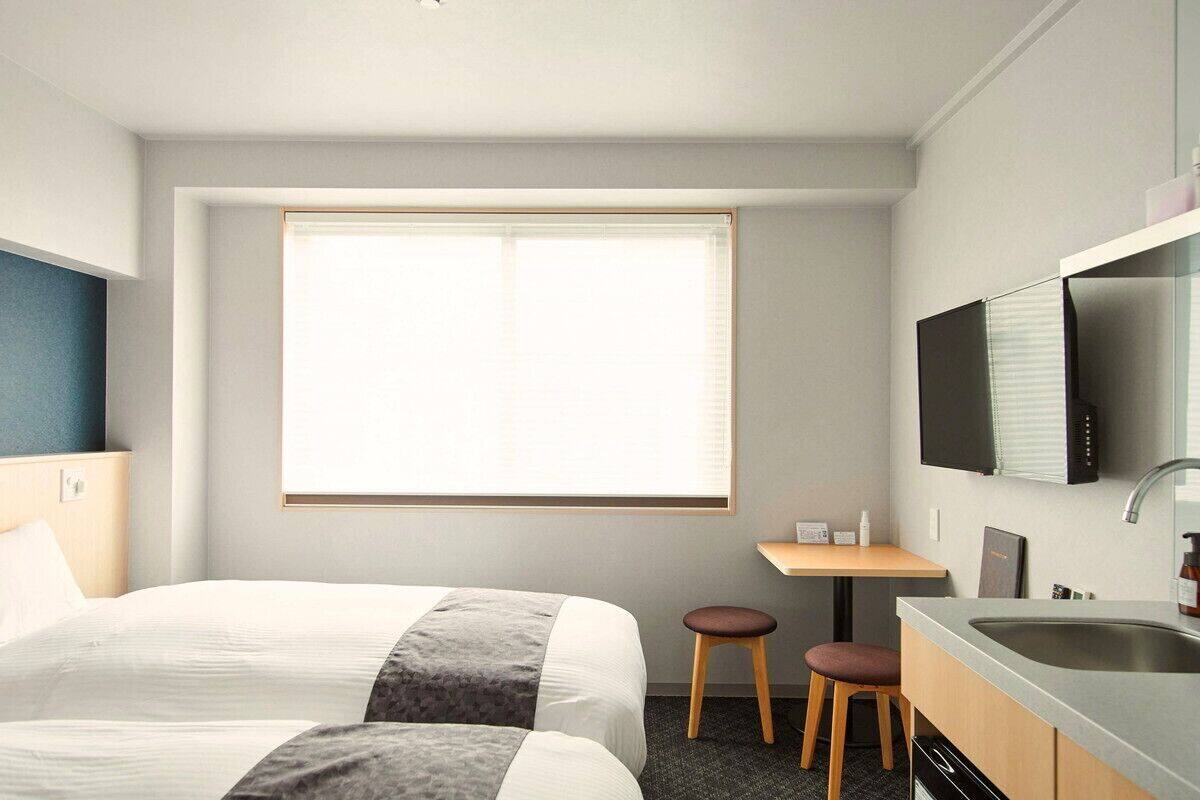 Une chambre d’hôtel avec deux lits, un bureau, un lavabo et une télévision.