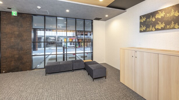 A reception area with a modern design, featuring a reception desk, seating area, and large windows providing a view of the street. - hotel GOCO stay Kyoto Shijo Kawaramachi (Kyoto)