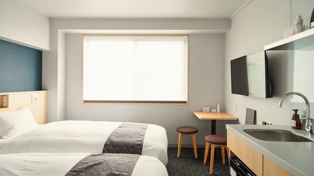 Une chambre d’hôtel avec deux lits, un petit bureau, un lavabo et un téléviseur fixé au mur.