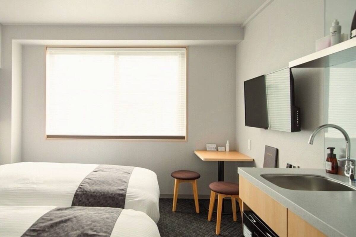 Une chambre d’hôtel avec deux lits, un petit bureau, un lavabo et un téléviseur fixé au mur.
