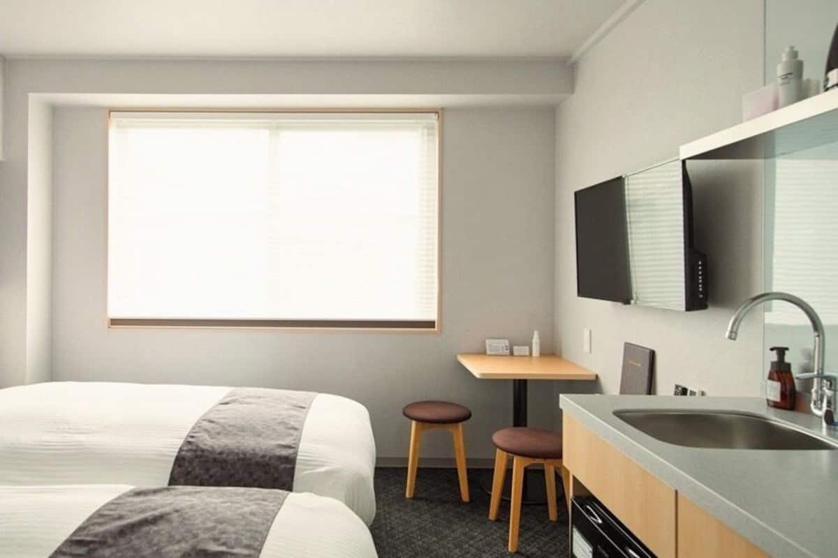 Une chambre d’hôtel avec deux lits, un petit bureau, un lavabo et un téléviseur fixé au mur.