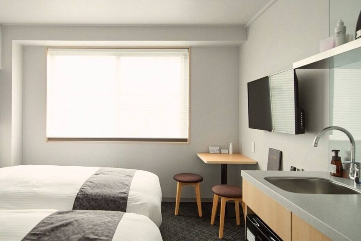 Une chambre d’hôtel avec deux lits, un petit bureau, un lavabo et une télévision.