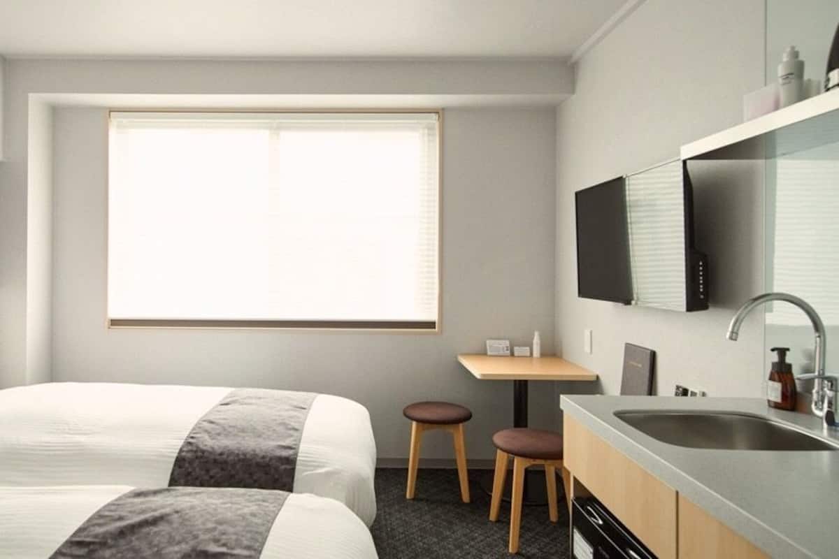 Quarto de hotel com duas camas, uma secretária pequena, pia e televisão.