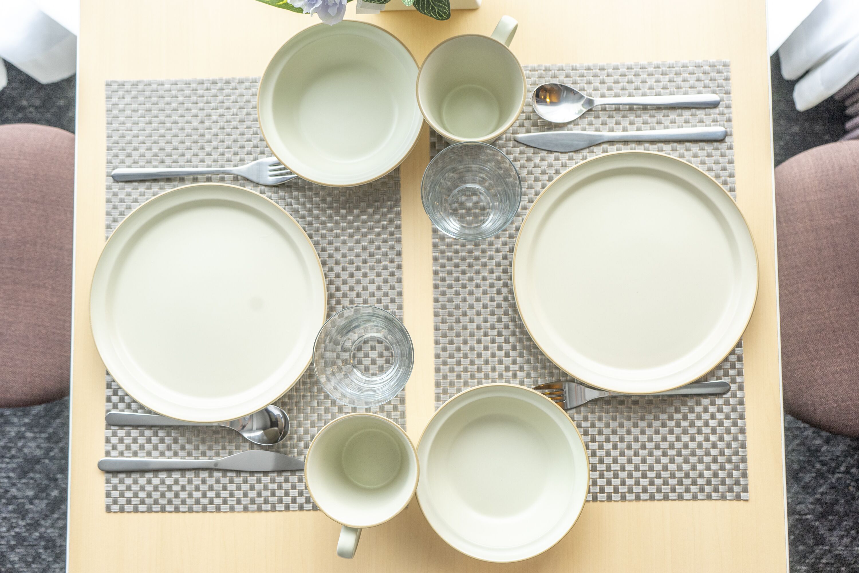 A table set with plates, bowls, cups, and cutlery, arranged on a woven placemat.
