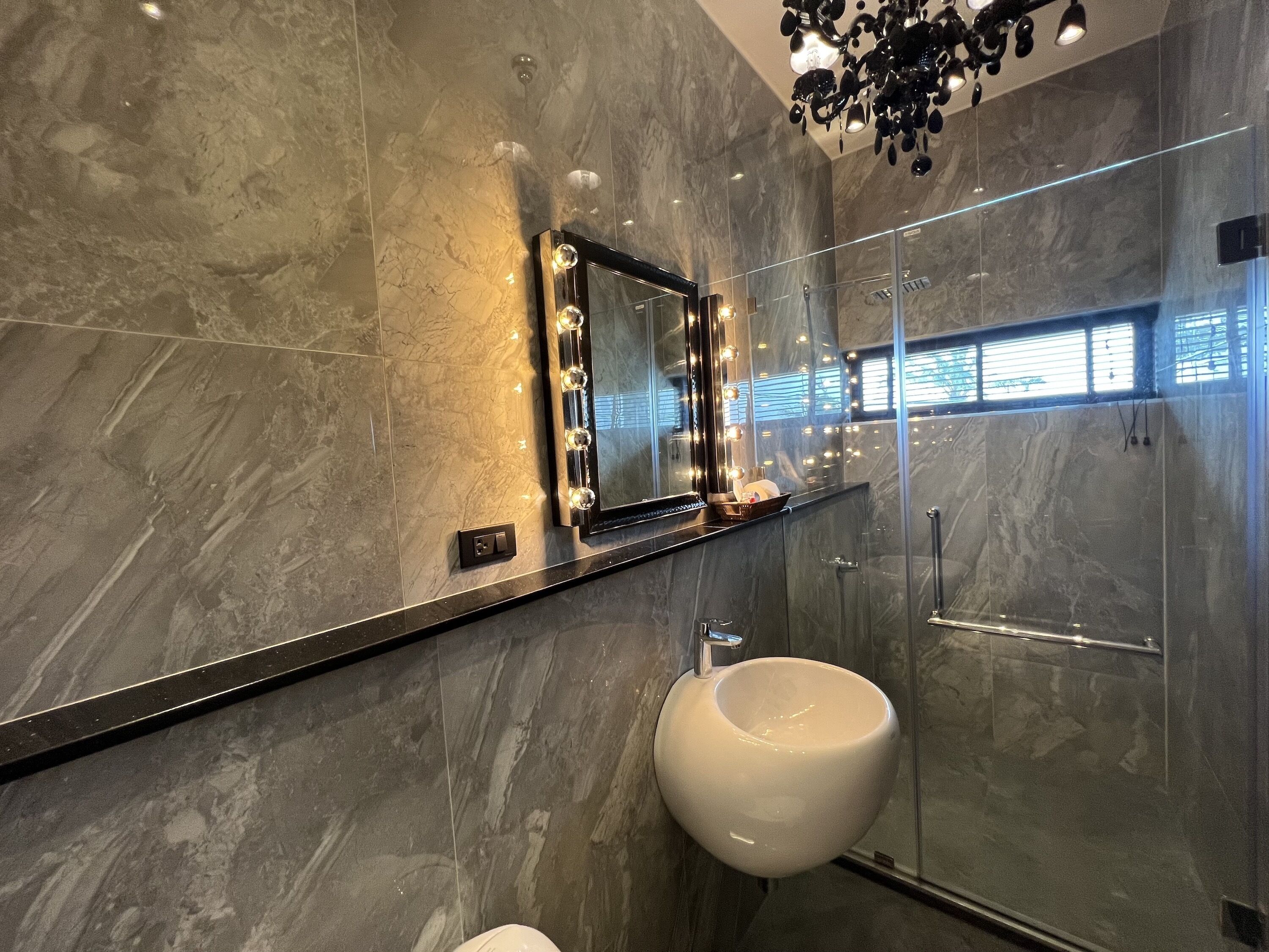 Een moderne badkamer met een marmeren wand, een wastafelmeubel met spiegel en verlichting, een witte wasbak en een glazen douchecabine.