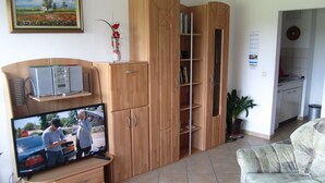 A living room with a television, wooden cabinets, a sofa, and a potted plant. - Ferienwohnungen an der Therme (Bad Rodach)