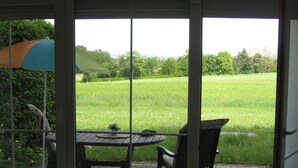 A patio with a table and chairs, a view of a green field through a glass door. - Ferienwohnungen an der Therme (Bad Rodach)