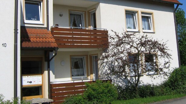 Ein zweistöckiges Wohngebäude mit Balkon, einer kleinen Veranda und der Hausnummer 10 an der Fassade.