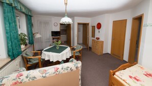 Ein gemütlicher Raum mit rundem Tisch, floralem Sofa, Holzstühlen, Deckenventilator und Holzschrank.