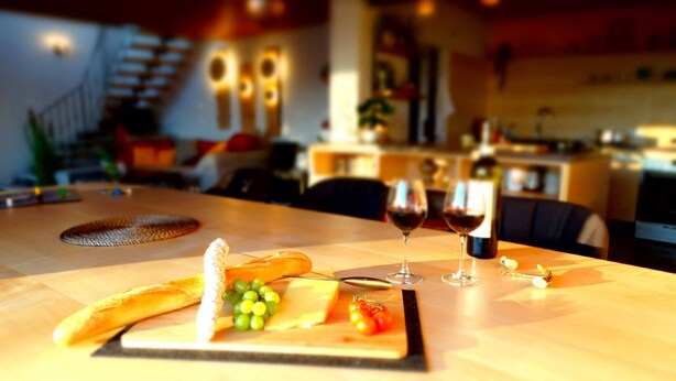 A dining table with a cheese board, grapes, tomatoes, and two wine glasses. - Ferienhaus Sine Tempo (Marktleugast)