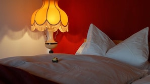 A bed with white linens, a decorative lamp, and a red wall in the background. - Ferienhaus Sine Tempo (Marktleugast)