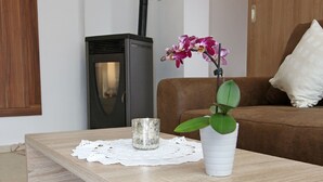 En moderne stue med et træbord, en hvid vase med en plante, en dekorativ glasvase, en sofa og en sort brændeovn.