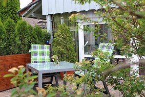 A patio with a table and chairs, surrounded by greenery and a building with a tiled roof. - Ferienwohnung Wandl (Bad Griesbach im Rottal)