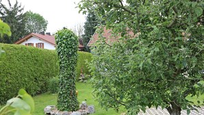 En have med en hæk, et træ og et hus i baggrunden.