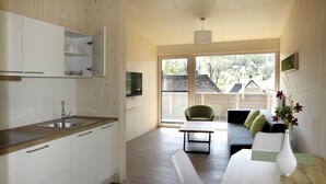 A modern kitchen with a wooden countertop, white cabinets, and a large window offering a view of a house and trees. - Steigerwald-Apartments (Ebrach)