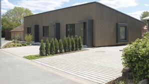 A modern building with a flat roof, large windows, and a paved driveway. - Steigerwald-Apartments (Ebrach)