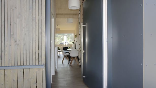 A hallway with wooden walls, a dark door, and a dining area with chairs and a table. - Steigerwald-Apartments (Ebrach)