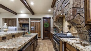 A kitchen with granite countertops, wooden cabinets, a stone accent wall, a built-in oven, and a microwave. - Entertainment Castle With Theatre Room! (Meridian)