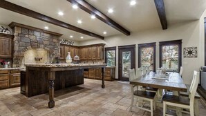A kitchen with a stone fireplace, wooden cabinets, and a dining area with a table and chairs. - Entertainment Castle With Theatre Room! (Meridian)