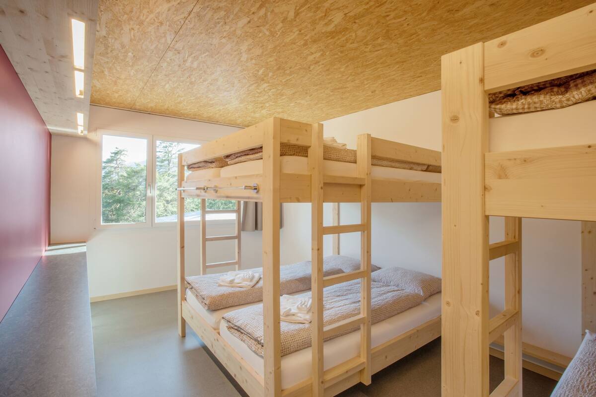 Camera con letto a castello, soffitto in legno e finestra che lascia entrare la luce naturale.