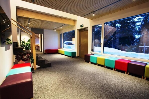 A modern interior with a staircase, colorful seating, and large windows with a snowy view. - Sport- und Ferienhaus Don Bosco (Lantsch-Lenz)